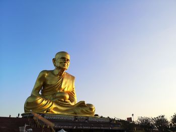 Low angle view of golden buddhist monk statue against sky in evening light