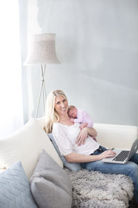 Woman holding newborn daughter and using laptop