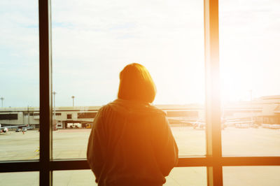 Rear view of woman standing by window at airport terminal