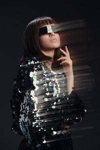 Portrait of young woman standing against black background