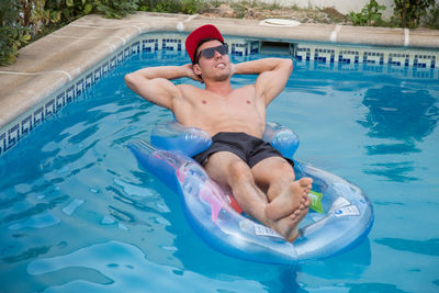 Shirtless young man relaxing on pool raft in swimming pool