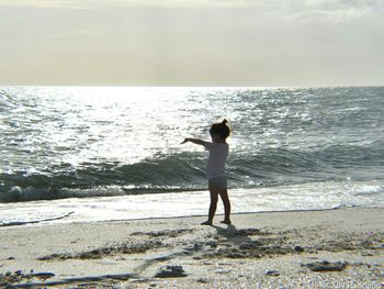 Rear view of boy standing on beach against sky