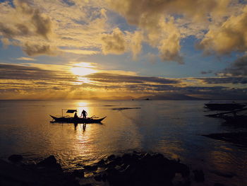 Silhouette man sitting in sea against sky during sunset