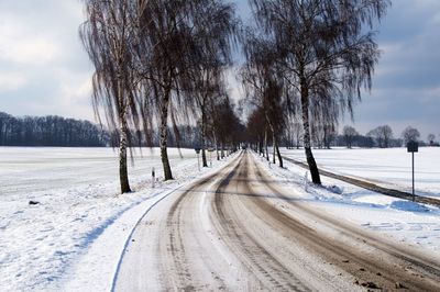 Snow covered road amidst field against sky