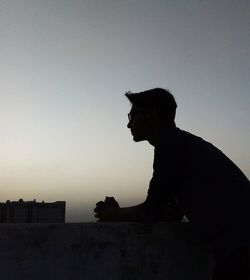Silhouette man sitting against clear sky during sunset