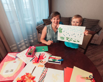 Mother and son drawing pictures together sitting by table in living room