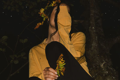 Close-up of woman sitting against tree at night