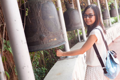 Portrait of young woman striking bell while standing outdoors