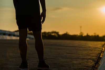 Low section of woman standing on shore against sky during sunset
