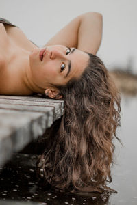 Close-up portrait of young woman lying down on pier over lake