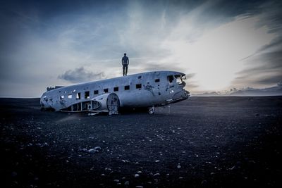 Abandoned airplane on sand against sky at sunset