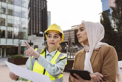 Engineer wearing hardhat discussing with businesswoman holding tablet pc