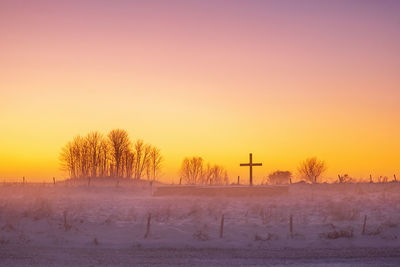 Snow covered field against sky during sunset