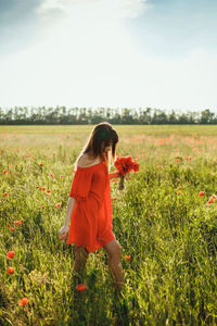 A girl in a red dress above the knee stands in a poppy field in the afternoon