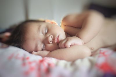 Close-up of cute naked baby girl sleeping on bed