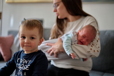 Mother with little toddler and newborn baby sitting on a sofa