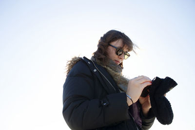 Low angle view of woman using mobile phone while standing against clear sky