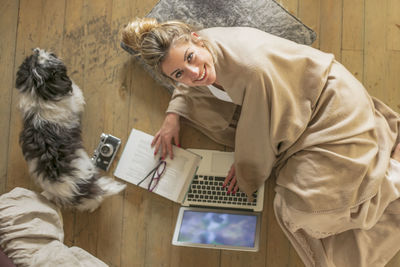 High angle view of young woman with dog using laptop on wooden floor