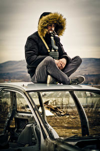 Full length of man sitting on abandoned car