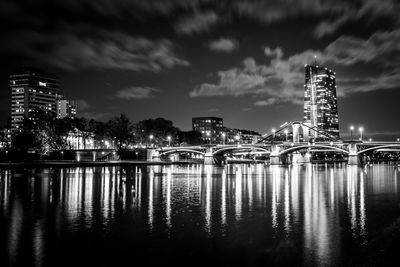 Bridge over river against buildings at night