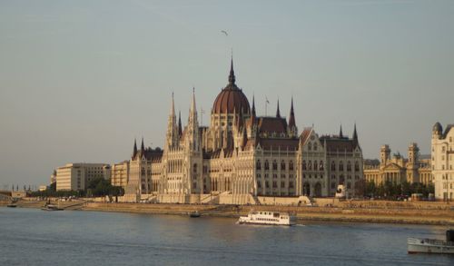 View of buildings by river against sky in city