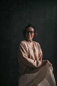 Portrait of smiling young woman standing against black wall