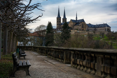 Empty bench on footpath by michaelsberg abbey against sky