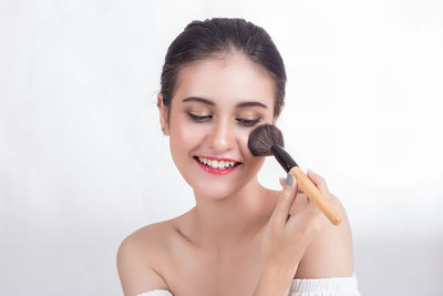 Smiling young woman applying make-up against white background