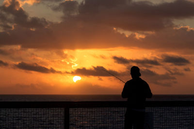 Rear view of silhouette man standing at sea during sunset