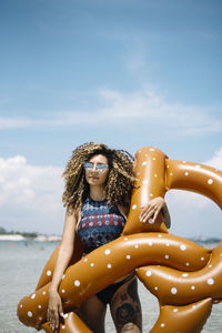 Portrait of smiling woman holding pool raft while standing at beach