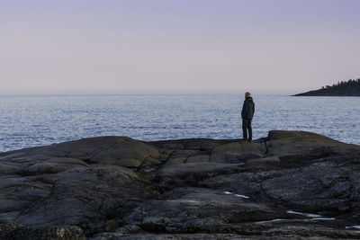 Man standing on rock by sea against sky