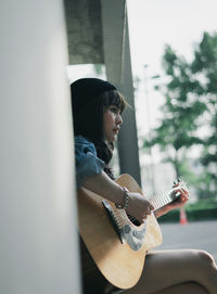 Young woman playing guitar on window