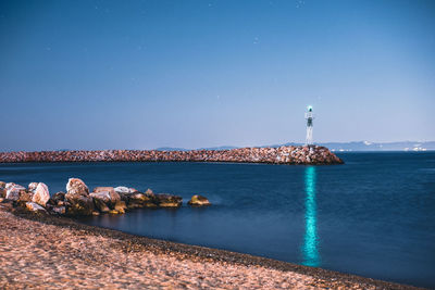 Lighthouse amidst sea and buildings against blue sky