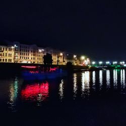 Illuminated buildings by river against sky at night