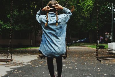 Rear view of woman showing middle fingers while sitting on swing at park