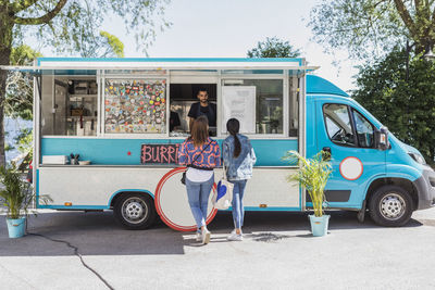 Full length rear view of female friends talking with male food truck owner in city on sunny day