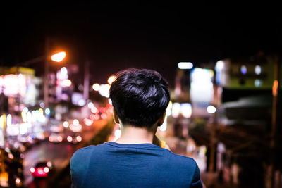 Rear view of man looking at illuminated city in night