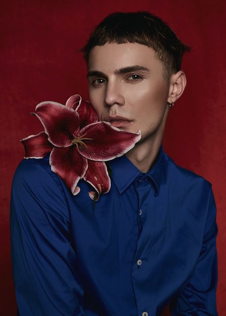 PORTRAIT OF YOUNG MAN WITH RED FLOWERS AGAINST WALL