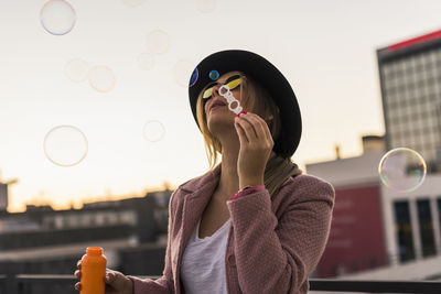 Young woman in the city blowing soap bubbles in the evening