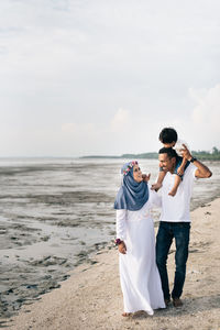 Happy family standing on shore at beach against sky