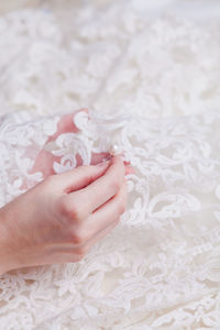 Cropped hand of woman stitching pearls on white wedding dress