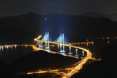 Illuminated bridge over river in city at night