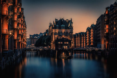 Bridge over river amidst buildings in city at dusk