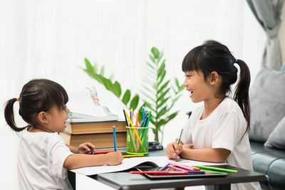 Siblings painting over paper on table