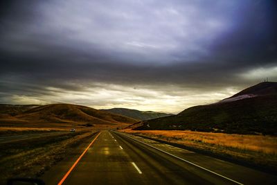 Road passing through landscape against dramatic sky