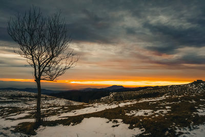 Snow covered landscape against sky during sunset