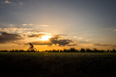Man cycling of field against sky during sunset