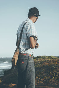 Rear view of man standing on rock against sky