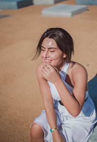 Smiling young woman looking while sitting on footpath during sunny day