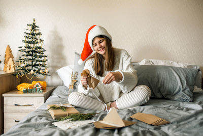 Smiling girl holding envelope sitting on bed at home